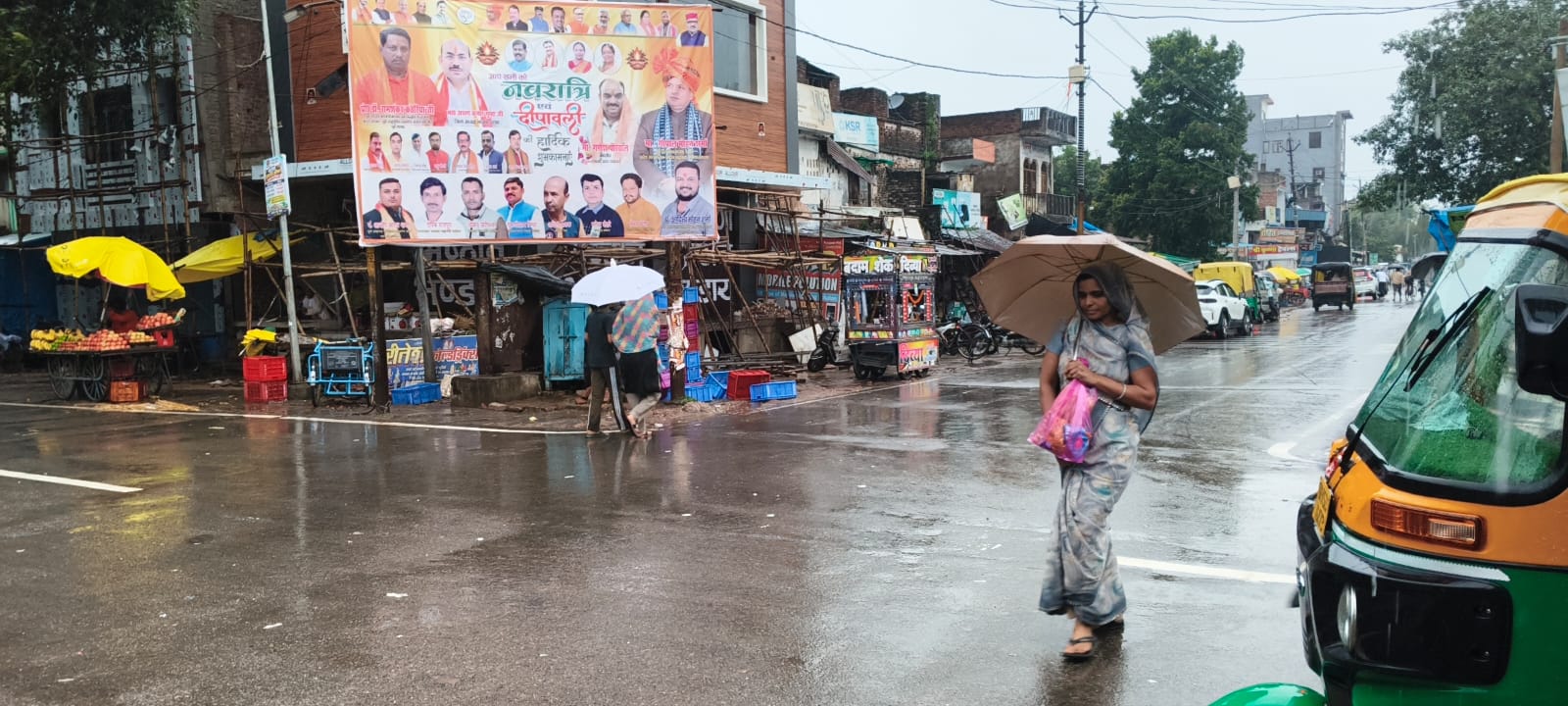 बारिश के दौरान बकेवर कस्बे के बाजार में छाता लगाकर जाते लोग